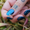 Tattooed fingers and blue polished nails showcase an X shaped diamond earring topper; by @lauralovesmetal