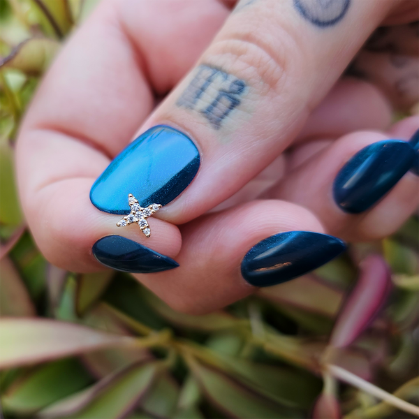 Tattooed fingers and blue polished nails showcase an X shaped diamond earring topper; by @lauralovesmetal